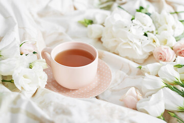 Fototapeta na wymiar Breakfast in bed in hotel room. Accommodation. Breakfast in bed with tea cup and flowers on bed background top view. Copy Space. Romantic valentine's day breakfast. Cozy morning. Happy Mother's Day