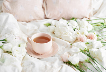 Fototapeta na wymiar Breakfast in bed in hotel room. Accommodation. Breakfast in bed with tea cup and flowers on bed background top view. Copy Space. Romantic valentine's day breakfast. Cozy morning. Happy Mother's Day