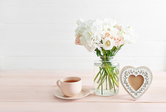 Bouquet of roses, eustomas and hydrangeas on table. Cup of tea and photo frame. Greeting card for mothers day. Cozy good morning. Happy Birthday. Romantic breakfast. Flowers composition for Valentine