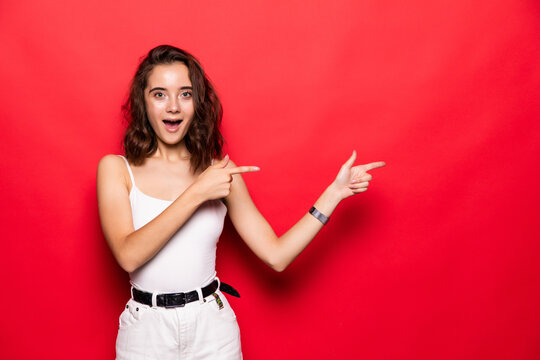 Young woman showing pointing on red background. Very fresh and energetic beautiful young girl smiling happy presenting on red background.