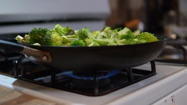Skillet full of freshly cut broccoli cooking on the stove top - slow motion
