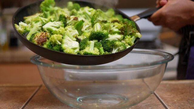 Carefully shaking a pan full of freshly cooked broccoli into a glass bowl - slow motion