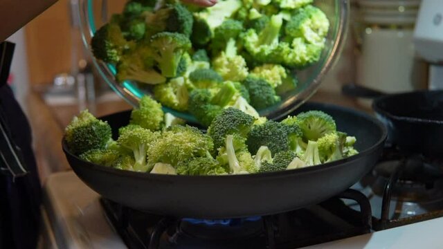 Filling a skillet with freshly cut broccoli to cook, fry or steam - slow motion