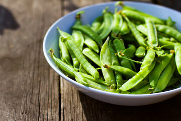 
Green pea pods in a white bowl on a wooden background with copy space, vegan food and healthy organic food concept. Harvesting.