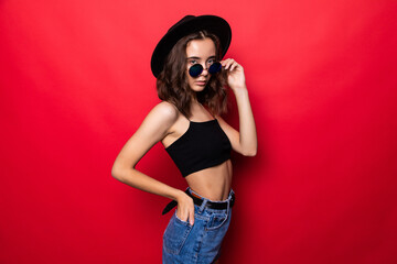 Young pretty woman in floppy hat and sunglasses standing isolated on red background