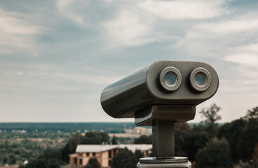 Touristic telescope overlooking city park. Metallic observation binoculars closeup with left copy space. Toned