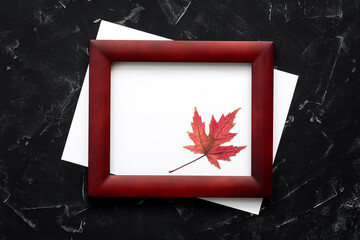 Blank paper and wood frame decorated with a maple leaf on a black stone background. Modern minimal invitation mockup. Top view, flat lay.