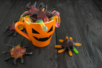 Orange cup with candy for Halloween on black surface. Copy space.