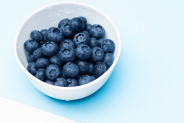 Blueberry in bowl with water drops on a blue background.