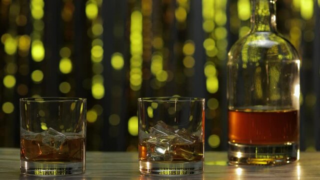 Barman pushes, puts two glasses with golden whiskey, cognac or brandy with ice cubes on wooden table