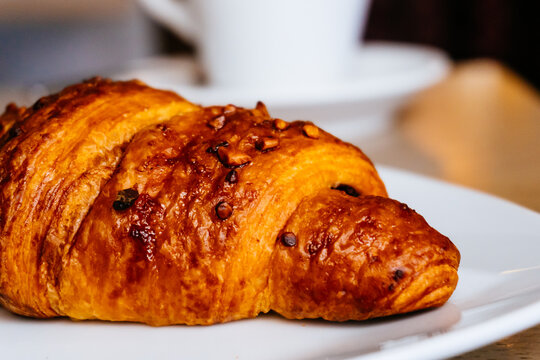 Croissant filled with chocolate and decorated with hazelnuts, at the bottom cup of hot coffee. © Manuel Milan