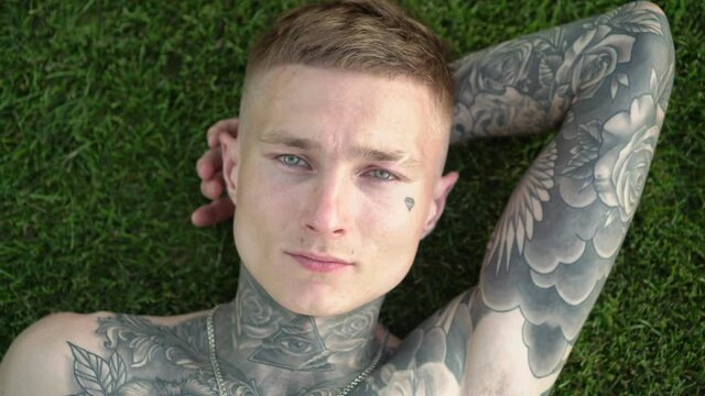 Young attractive male model with tattoos lies on the green grass in the park