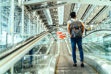 New normal and Travel insurance concept.Young caucasian man wearing face mask and carrying backpack on escalator or travelator walkway in airport terminal,protection during coronavirus pandemic.