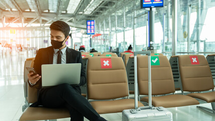 New normal and social distance concept.Business man wearing mask using smartphone searching airline flight status and sitting with distance during corona virus 2019 outbreak at airport