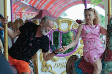 Caucasian Senior couples holding hands while playing carousel at the amusement park
