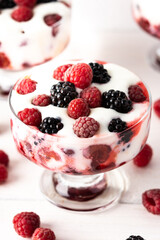 Delicious juicy berries of raspberries and blackberries with yoghurt in a glass form on a white background