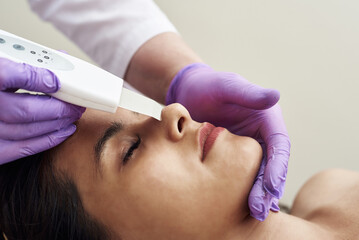 A woman makes an ultrasonic cleaning of the face and skin to a client. Modern equipment. Young pretty woman receiving treatments in beauty salons and lying on the couch