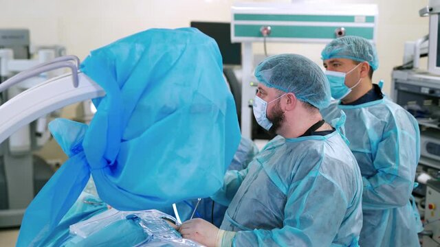 Doctors conduct a surgery. Medical workers in blue protective uniform work in the operating room in clinic. Surgical procedure in operating theater.