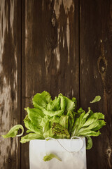 Lettuce leaveson in a paper bag a wooden dark table. Batavia salad. Authentic still life with green salad flat lay. Rustic style Top view
