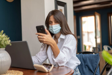 Beautiful young woman working on laptop computer, looking in her smart phone.