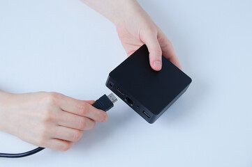 Hands of caucasian woman connects hdmi cable TV box  black box. White background.