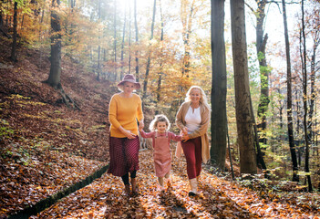 Small girl with mother and grandmother on a walk in autumn forest.