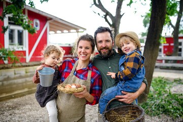 Fototapeta premium Portrait of family with small children standing on farm, holding basket with eggs.