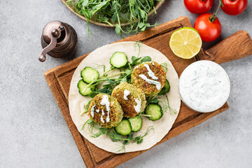 Vegan falafel with vegetables and tzatziki sauce on wooden board, top view. Arabic food