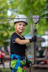 Fototapeta na wymiar a little boy in a rope Park in a protective helmet and ammunition goes forward to victory