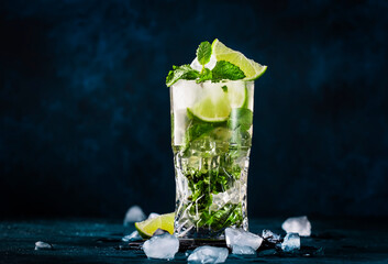 Mojito cocktail or mocktail with lime, mint, and ice in glass on blue background. Summer cold alcoholic non-alcoholic drink,  beverage and cocktail. Copy space - obrazy, fototapety, plakaty