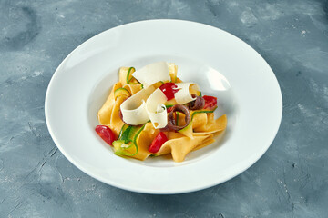 Italian pasta with vegetables, parmesan and anchovies in a white bowl on a concrete background