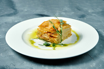 Baked potato gratin with cream and cheese in a white plate on a concrete background