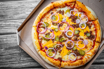 Pizza with Mozzarella cheese, Bolognese sauce, minced meat and vegetables. Italian pizza in paper box on wooden background.