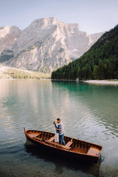 Beautiful couple in love hugs and kisses standing on wooden boat in the middle of mountain lake