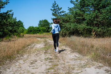 Young fit beautiful girl running outdoor on a dirt road during summer sunny day