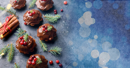 Fototapeta na wymiar Christmas chocolate cupcakes, with icing, are decorated with a sprig of spruce, and cranberries. On a dark table dessert, with cinnamon sticks, snowflakes, serpentine.