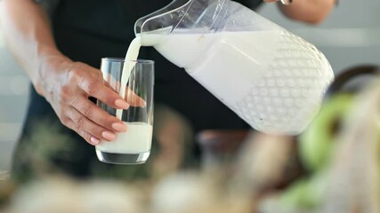 Closeup female hands pouring homemade milk from jug into glass. Shot on RED Raven 4k Cinema Camera