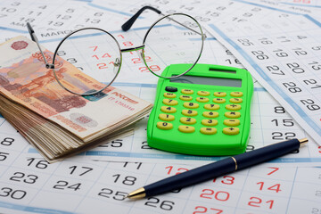 Money, calculator, glasses and pen are on the calendar