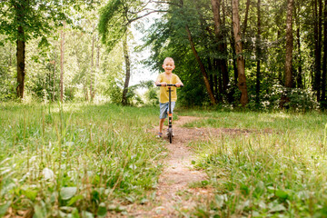 Little boy riding a scooter in road in park. child learning to ride a scooter outdoors. Active...