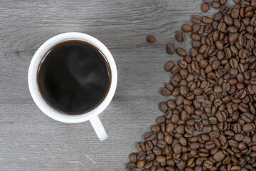 Grains of coffee with a cup of coffee on a wood background.