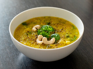 Hot vegan yellow curry soup with healthy vegetables and green salad in a white bowl close up detail