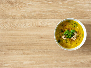 Hot vegan yellow curry soup with healthy vegetables and green salad in a white bowl top down view with bright wooden texture background