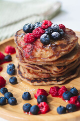 A heap of healthy vegan gluten-free whole grain pancakes made with buckwheat flour topped with raspberries and blueberries with icing sugar sprinkled on top 