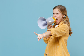Little blonde kid girl 12-13 years old in yellow jacket posing isolated on pastel blue background. Childhood lifestyle concept. Mock up copy space. Screaming in megaphone, pointing index finger aside.