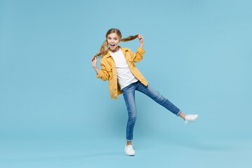 Obraz premium Pełnej długości portret podekscytowanej małej blond dziewczynki w wieku 12-13 lat w żółtej kurtce, pozowanie na białym tle na tle niebieskiej ściany studio. Koncepcja stylu życia dzieciństwa. Makieta miejsca na kopię. Trzymaj kucyki.