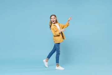 Obraz na płótnie Canvas Full length portrait side view of excited little kid girl 12-13 years old in yellow jacket isolated on blue background. Childhood lifestyle concept. Mock up copy space. Pointing index fingers aside.
