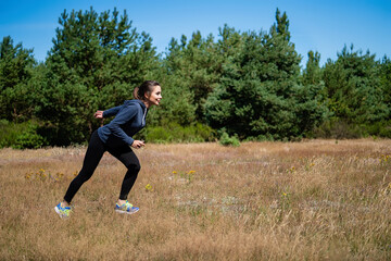 Young woman running on a natural meadow in the background of green trees and blue sky