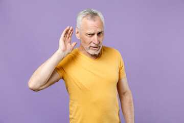 Curious elderly gray-haired bearded man in casual yellow t-shirt isolated on pastel violet...