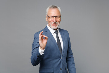 Smiling elderly gray-haired mustache bearded business man in classic blue suit shirt tie posing isolated on grey wall background studio. Achievement career wealth business concept. Showing Ok gesture.