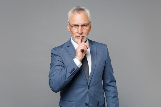 Secret elderly gray-haired bearded business man in blue suit shirt tie isolated on grey background . Achievement career wealth business concept. Saying hush be quiet with finger on lips shhh gesture.